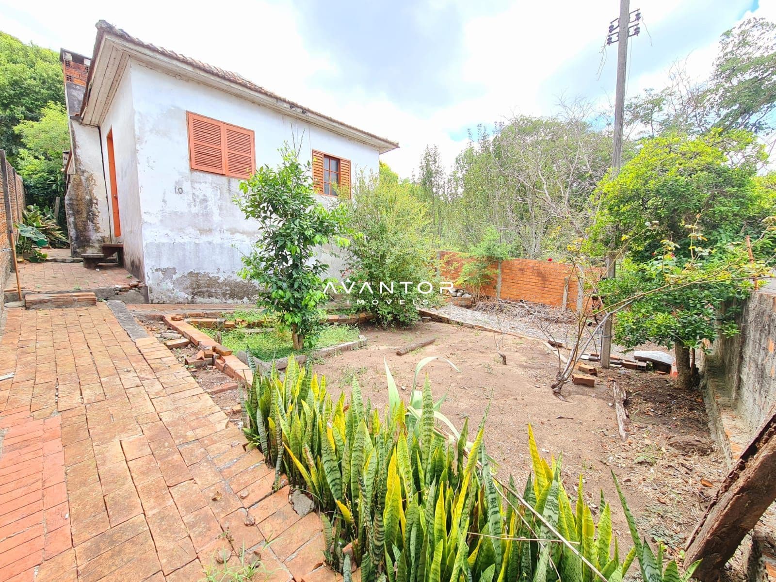 Fachada da casa com pátio e plantação — Terreno à venda em Nossa Senhora de Lourdes, Santa Maria/RS